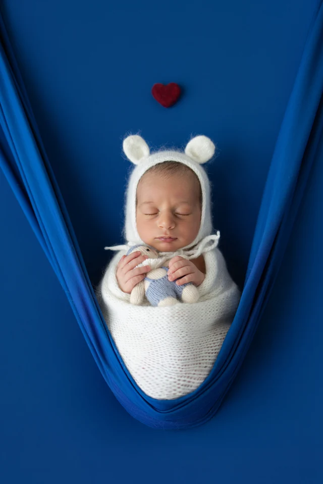 Newborn in a blue wrap with a small red heart in the setup
