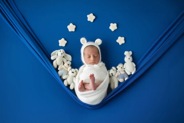 Newborn in a white wrap within a blue setup with stars and soft toys
