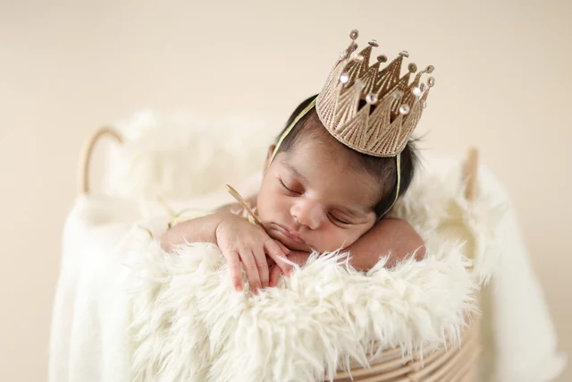Sleeping newborn in a cream basket with a crown, photographed by TALA