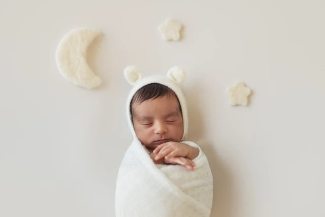 Newborn in a white wrap with a cream moon and stars