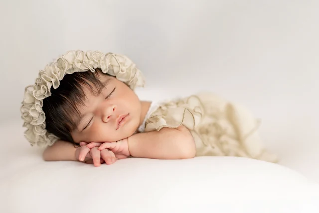 Sleeping baby wearing a cream floral headband on a light background