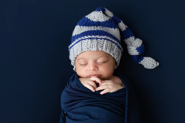Close newborn portrait with a knitted blue hat and navy wrap