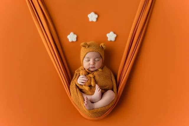 Newborn with a warm-coloured hat and wrap in an orange setup