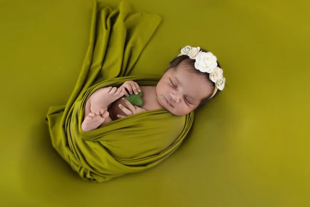 Baby in a green wrap and floral headband against a green background
