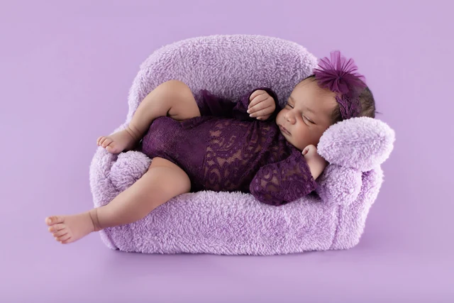 Baby resting on a small violet sofa in a styled portrait
